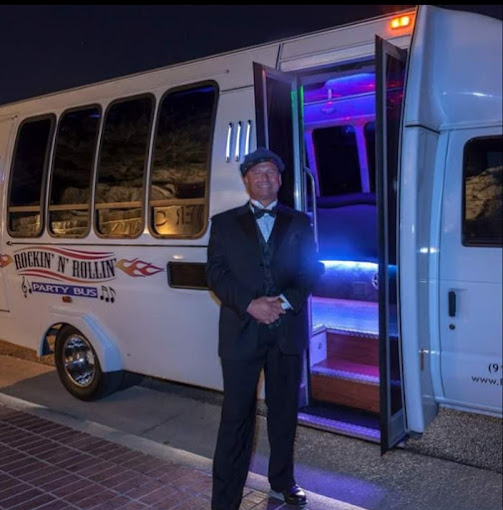 A man in a suit and hat standing next to a bus.