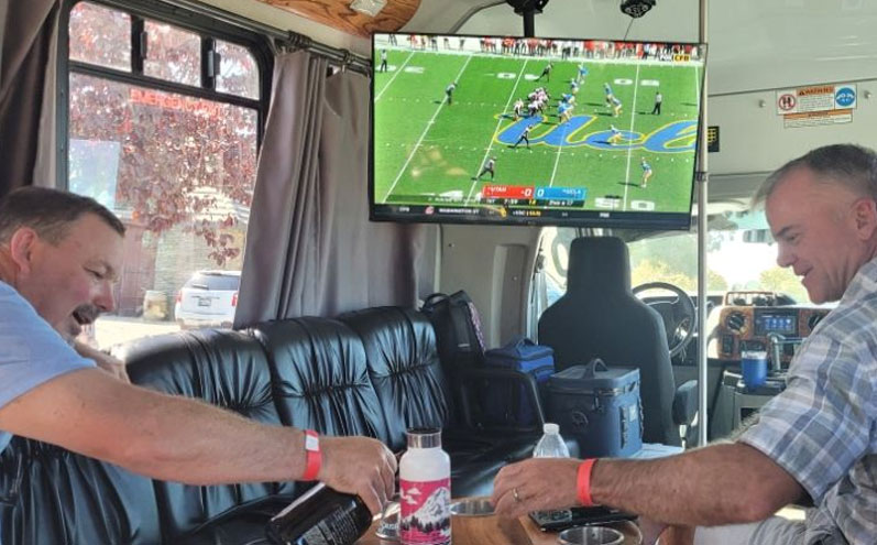 Two men sitting in a bus watching football.