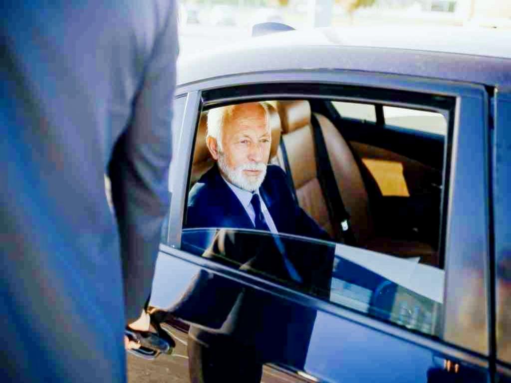 A man in a suit and tie sitting inside of a car.